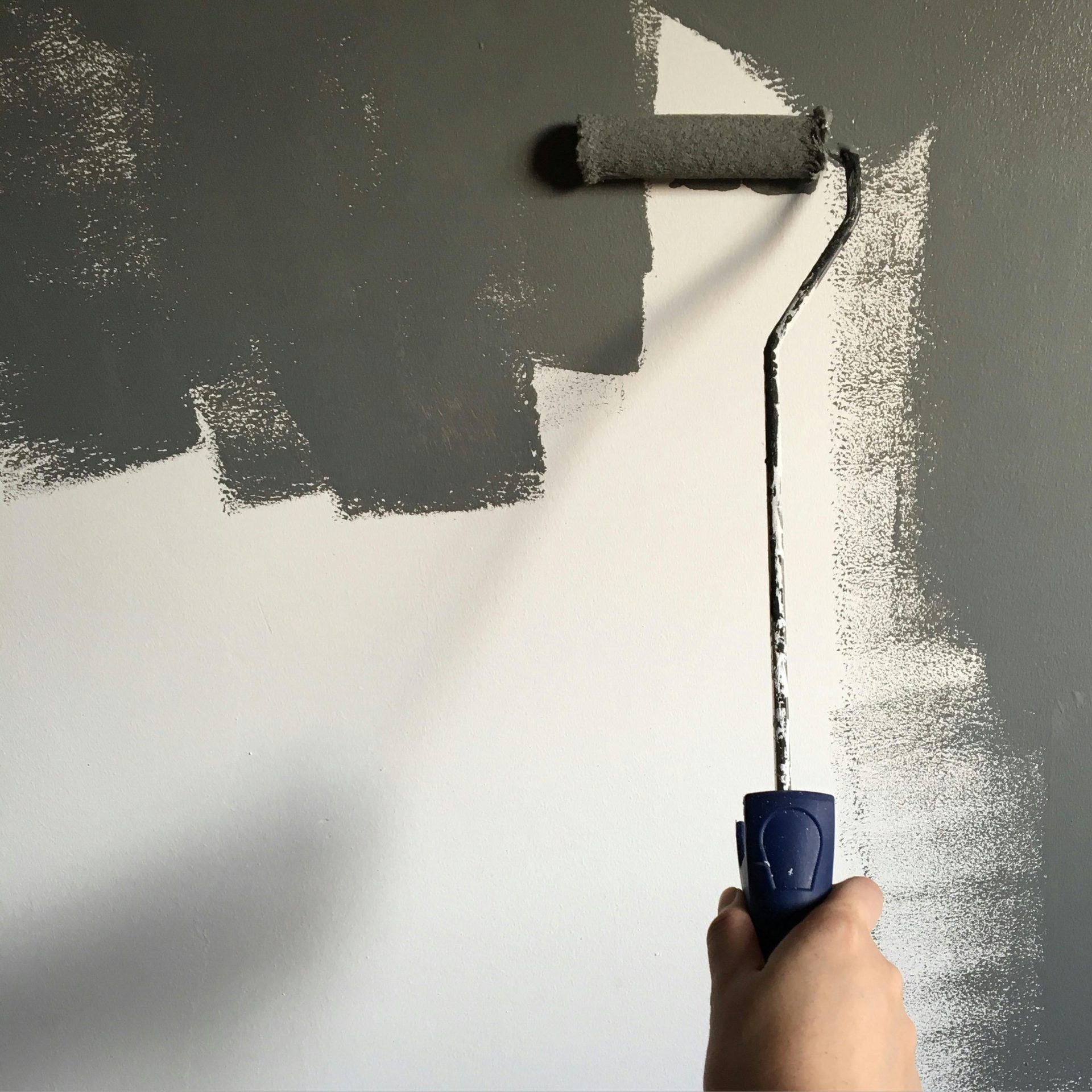 Eine Hand streicht im Rahmen einer Hausrenovierung mit einer Farbrolle eine Wand grau.